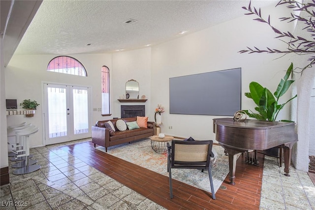 living area with a textured ceiling, a fireplace, visible vents, french doors, and wood tiled floor