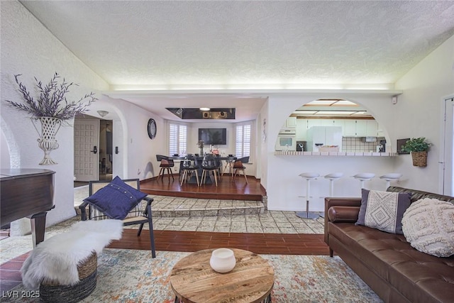 living room featuring lofted ceiling, arched walkways, a textured ceiling, and wood finished floors