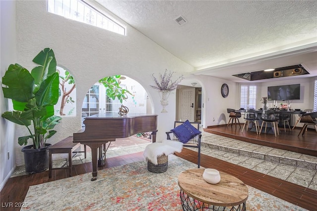 living area with visible vents, arched walkways, lofted ceiling, dark wood-type flooring, and a textured ceiling