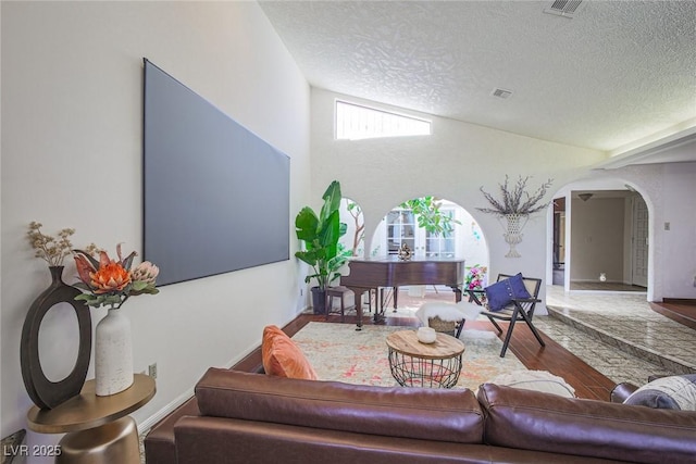 living area featuring baseboards, arched walkways, visible vents, wood finished floors, and a textured ceiling