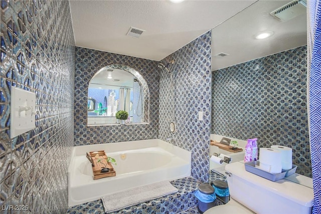 bathroom with a garden tub, tile walls, visible vents, and a textured ceiling