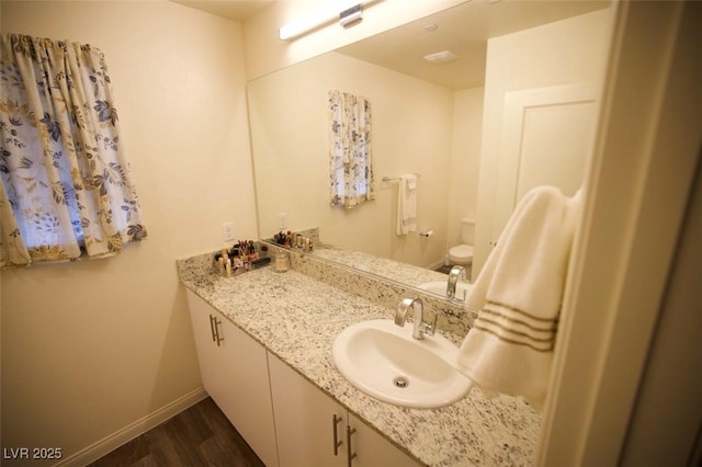 bathroom with toilet, wood finished floors, vanity, and baseboards