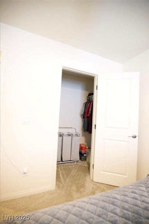 bedroom with a walk in closet, light carpet, and baseboards