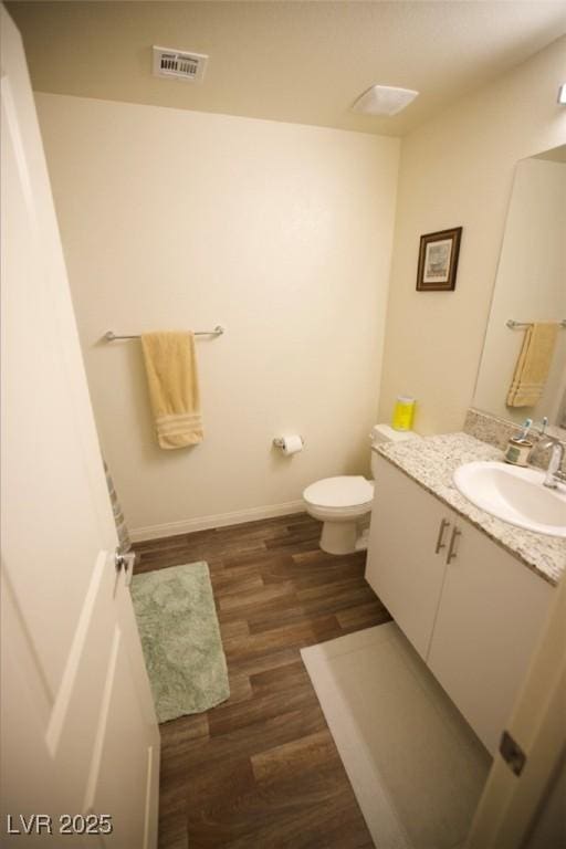 bathroom with baseboards, visible vents, toilet, wood finished floors, and vanity