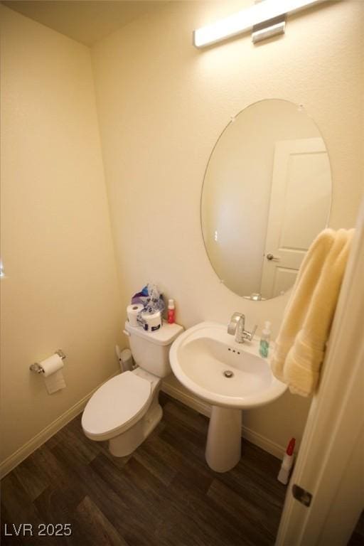 half bath featuring a sink, wood finished floors, toilet, and baseboards