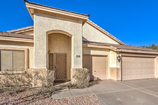 property entrance featuring driveway, a tiled roof, an attached garage, and stucco siding