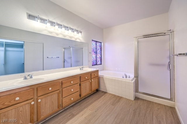 bathroom with a sink, wood finished floors, a shower stall, a bath, and double vanity