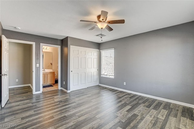 unfurnished bedroom featuring ensuite bathroom, dark wood-style flooring, visible vents, baseboards, and a closet