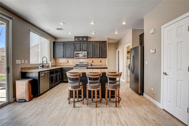 kitchen featuring a center island, a breakfast bar area, backsplash, appliances with stainless steel finishes, and a sink