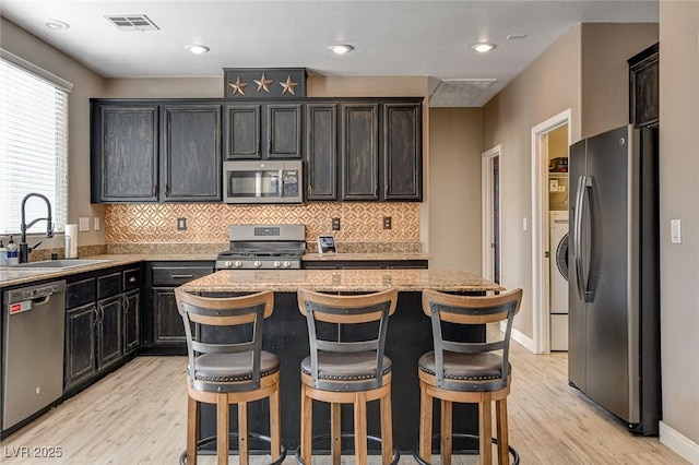 kitchen with light stone counters, a breakfast bar area, stainless steel appliances, a sink, and a kitchen island