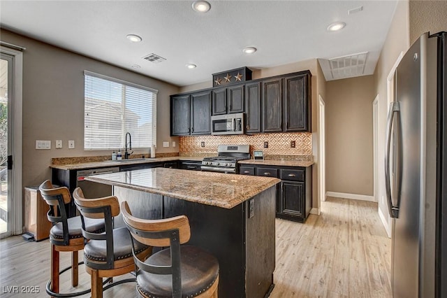 kitchen featuring a kitchen island, light stone counters, a breakfast bar, stainless steel appliances, and a sink