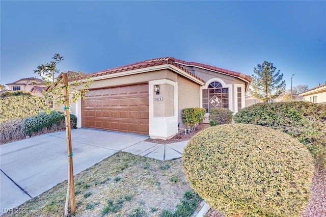 mediterranean / spanish house with concrete driveway, an attached garage, a tile roof, and stucco siding