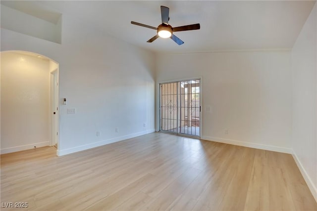 empty room with light wood finished floors, baseboards, arched walkways, a ceiling fan, and vaulted ceiling