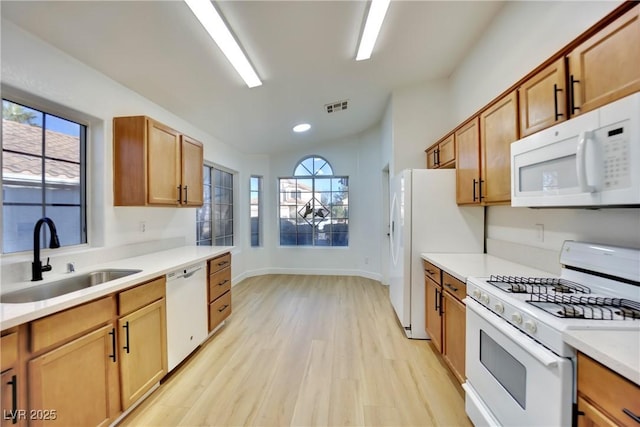 kitchen featuring white appliances, brown cabinets, light countertops, light wood-type flooring, and a sink