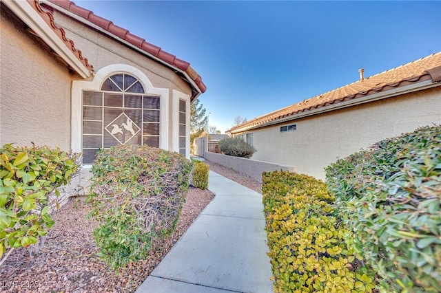 view of side of home with fence, a tiled roof, and stucco siding