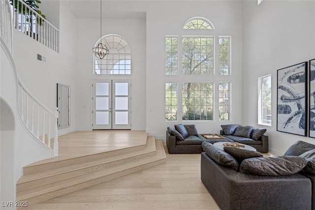 living area featuring a notable chandelier, visible vents, a high ceiling, light wood-type flooring, and stairs