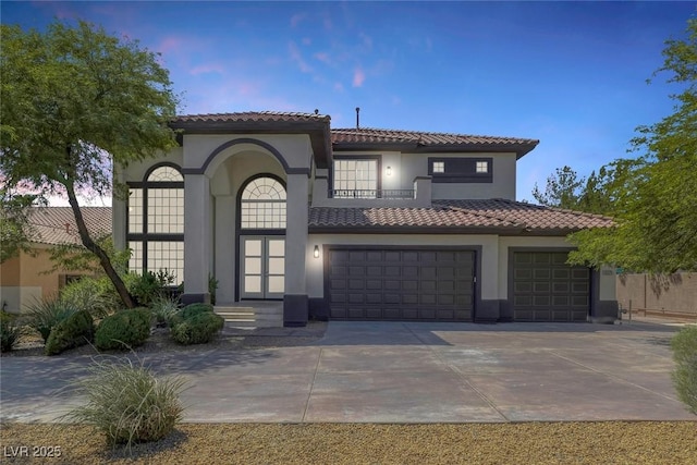 mediterranean / spanish home featuring concrete driveway, an attached garage, a tiled roof, and stucco siding