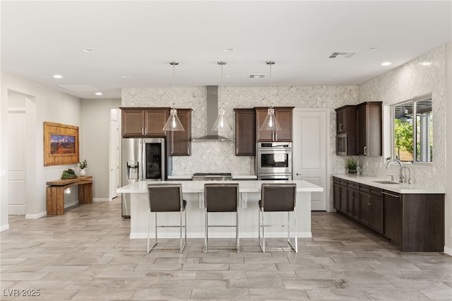 kitchen with wall chimney exhaust hood, a kitchen island, appliances with stainless steel finishes, light countertops, and a sink