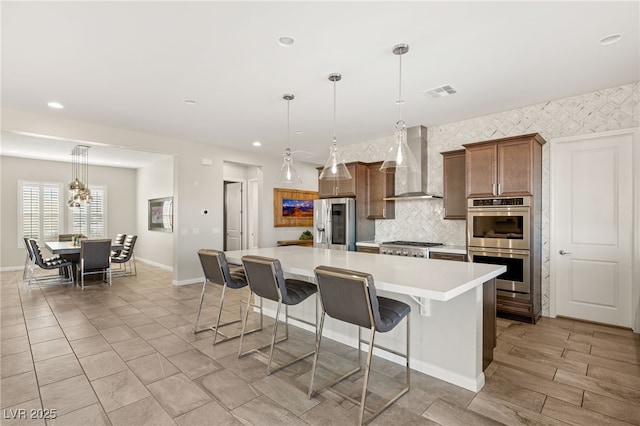 kitchen featuring a spacious island, visible vents, light countertops, appliances with stainless steel finishes, and wall chimney exhaust hood