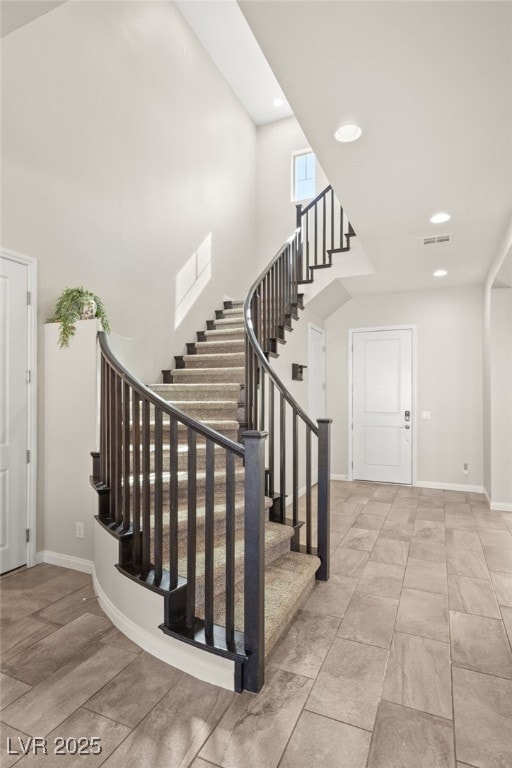 stairway featuring baseboards, a high ceiling, visible vents, and recessed lighting