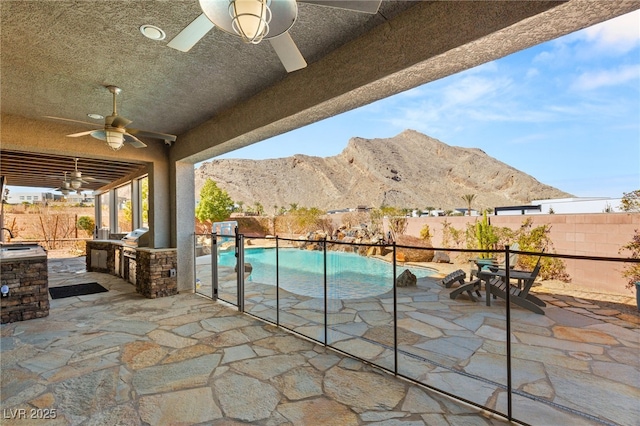 view of patio featuring a fenced in pool, a fenced backyard, a mountain view, and an outdoor kitchen