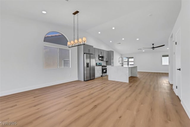 unfurnished living room featuring baseboards, light wood-style flooring, vaulted ceiling, a sink, and ceiling fan with notable chandelier