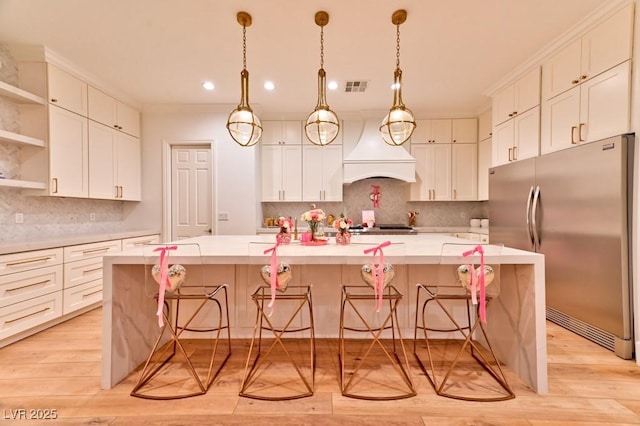 kitchen featuring a large island, custom exhaust hood, stainless steel refrigerator, and light countertops