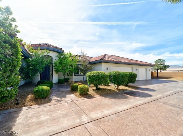 mediterranean / spanish house featuring a garage, concrete driveway, a tile roof, and stucco siding