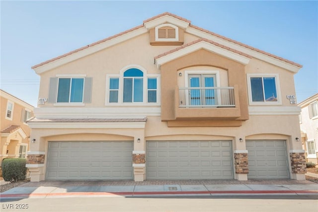 view of property featuring an attached garage, stone siding, a tiled roof, and stucco siding