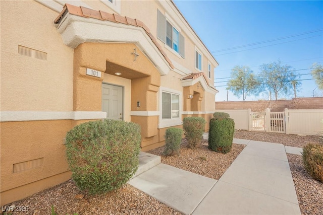 property entrance featuring a tile roof, fence, visible vents, a gate, and stucco siding