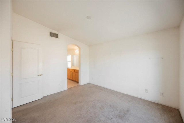 empty room with arched walkways, lofted ceiling, visible vents, and light colored carpet