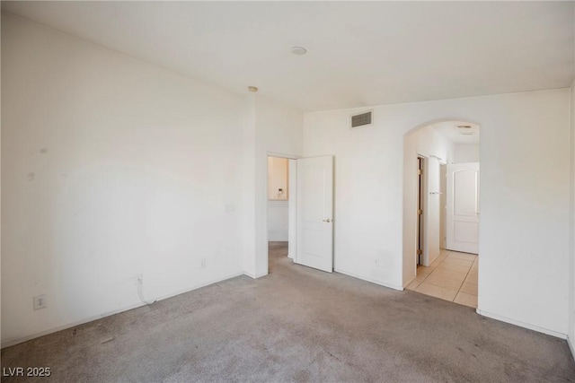 carpeted spare room with visible vents and arched walkways