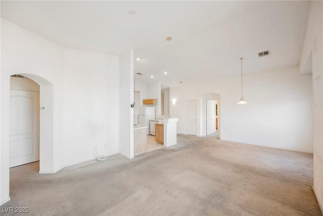 unfurnished living room with light carpet, visible vents, and arched walkways