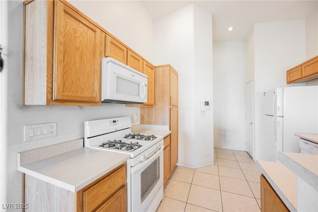 kitchen featuring light countertops, white appliances, light tile patterned flooring, and a towering ceiling