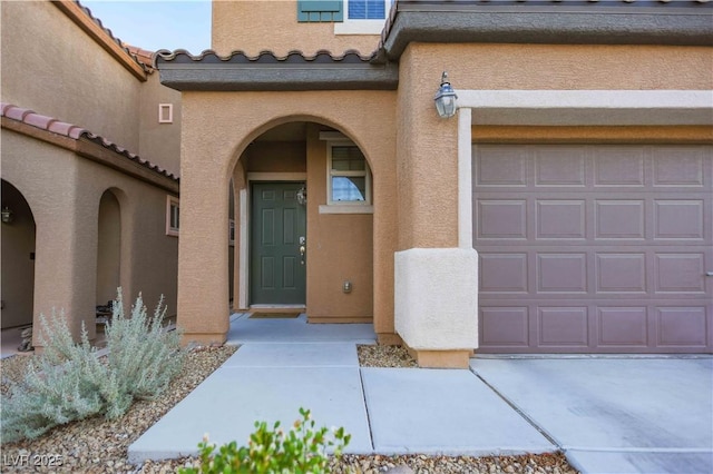 view of exterior entry featuring a garage, a tiled roof, and stucco siding