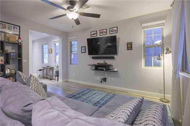 living room with a ceiling fan, visible vents, light wood-style flooring, and baseboards