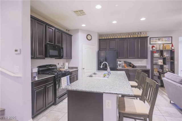 kitchen featuring visible vents, a sink, black appliances, an island with sink, and a kitchen breakfast bar