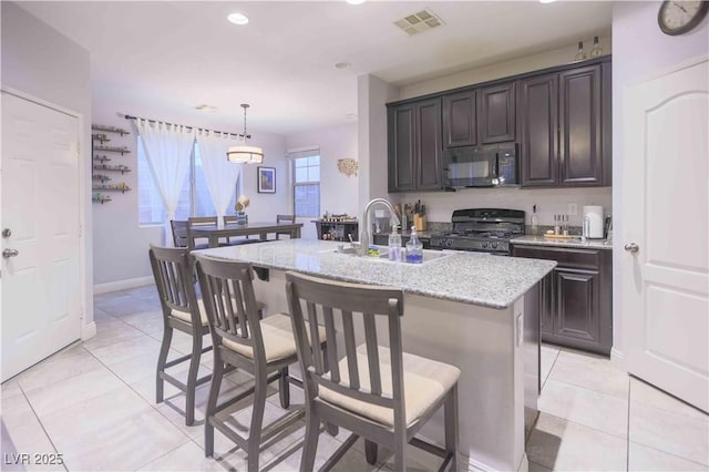 kitchen with a sink, visible vents, black appliances, an island with sink, and decorative light fixtures