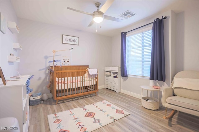 bedroom featuring light wood-style flooring, a crib, visible vents, and baseboards