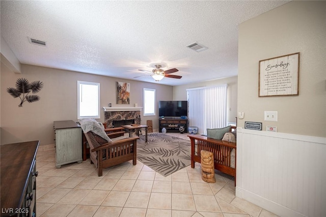 living area with light tile patterned floors, ceiling fan, a fireplace, and visible vents