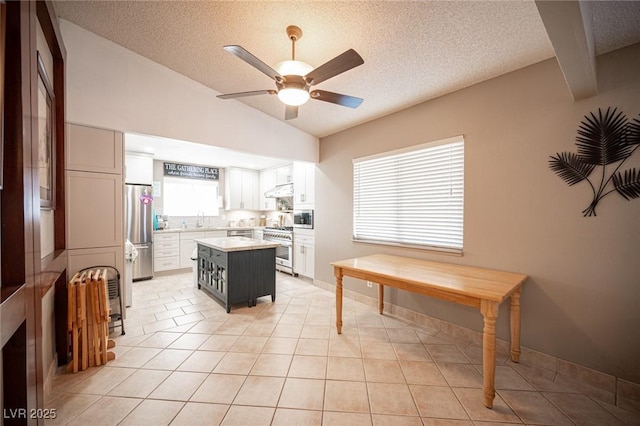 kitchen with a kitchen island, white cabinetry, vaulted ceiling, light countertops, and appliances with stainless steel finishes