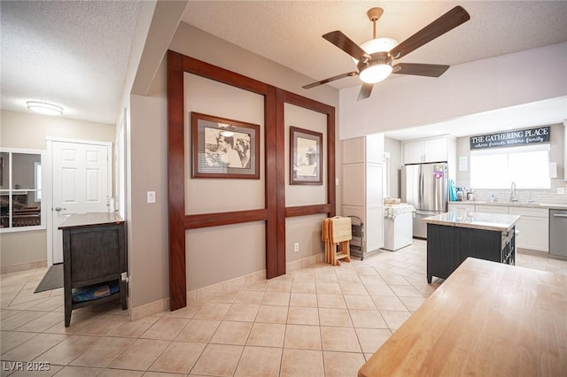 kitchen with stainless steel appliances, a sink, a kitchen island, white cabinetry, and light countertops