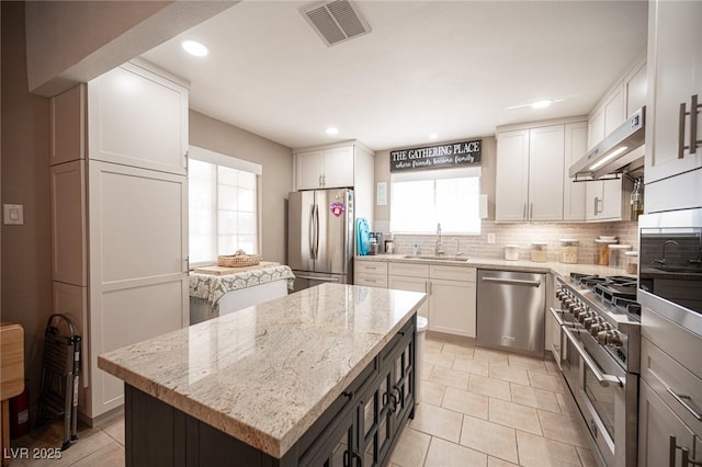 kitchen featuring a center island, stainless steel appliances, visible vents, a sink, and under cabinet range hood