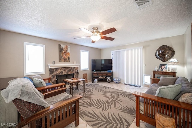 living area featuring light tile patterned floors, a premium fireplace, visible vents, and a ceiling fan