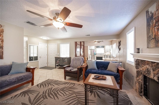 living room featuring light tile patterned floors, a textured ceiling, a fireplace, and visible vents