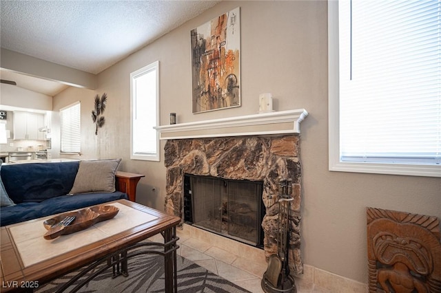 living area featuring light tile patterned flooring, a stone fireplace, and a textured ceiling