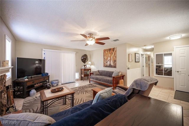 living room with a textured ceiling, light tile patterned flooring, a fireplace, visible vents, and a ceiling fan