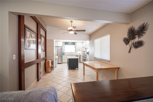 interior space with light tile patterned floors, appliances with stainless steel finishes, white cabinets, a kitchen island, and plenty of natural light