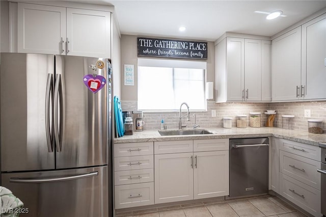 kitchen with light stone countertops, decorative backsplash, stainless steel appliances, and a sink