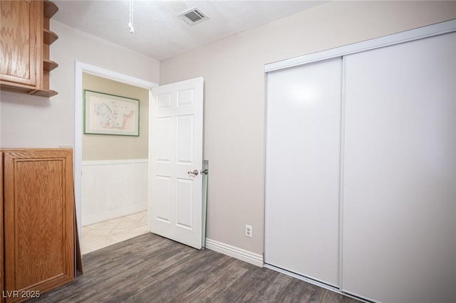 unfurnished bedroom with a wainscoted wall, a closet, dark wood finished floors, and visible vents